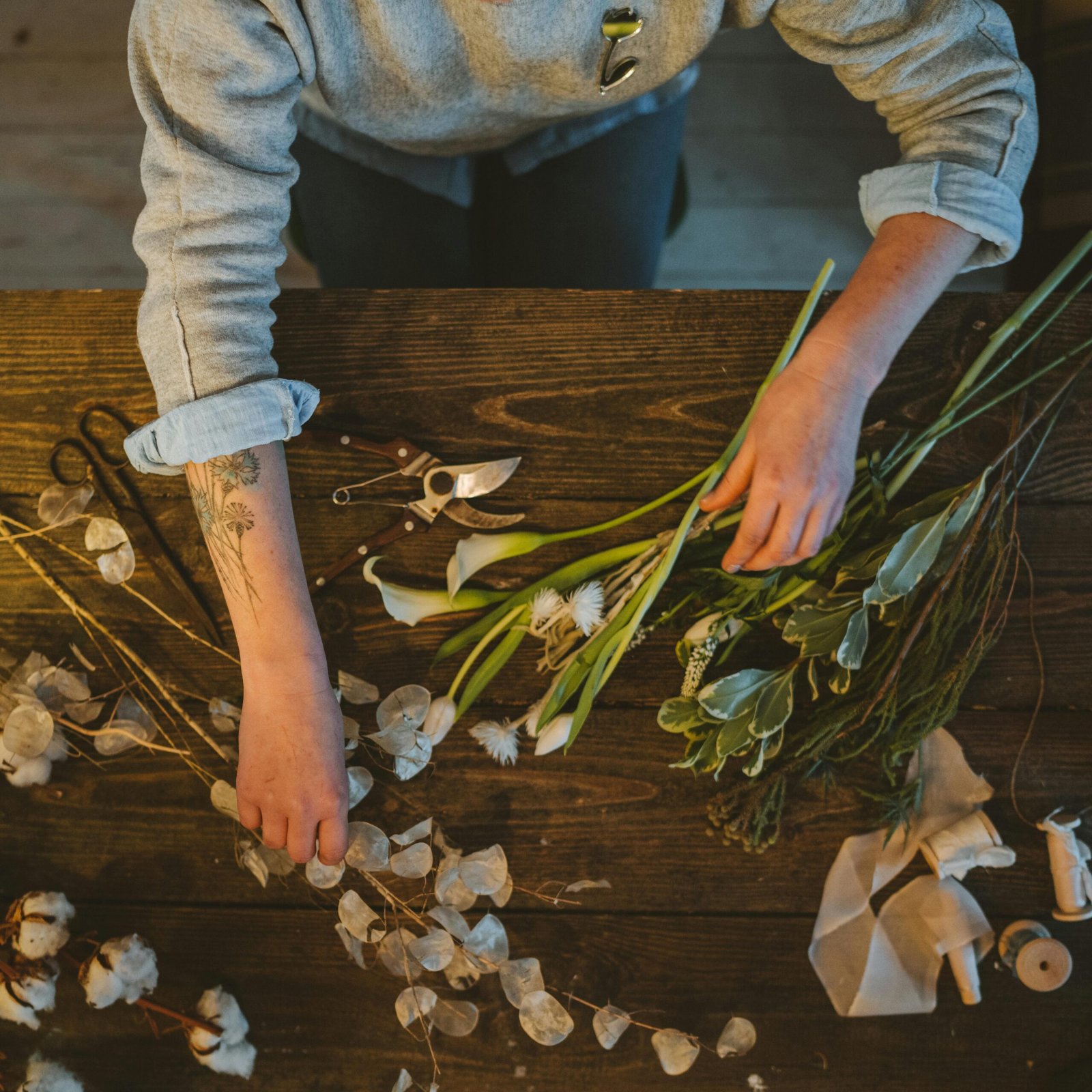 A detailed view of a florist arranging flowers on a rustic table, showcasing floral design artistry.